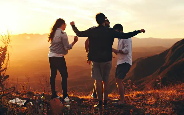 Junge Menschen tanzen auf einem Berg mit Sonnenuntergang im Hintergrund