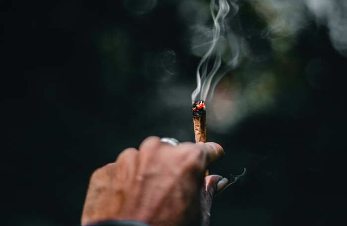 hand_haelt_qualmenden_joint_vor_dunklem_hintergrund
