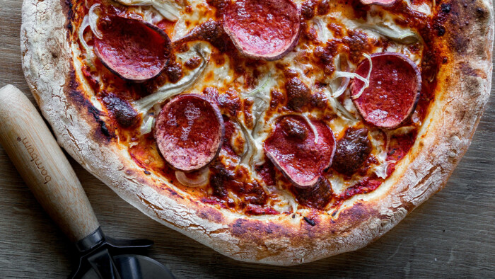 Salamipizza mit einem Pizzaroller im unteren linken Bildrand