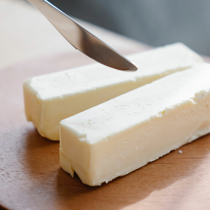 Ein Messer welches zwei Stücke Butter teilt auf einem Holzbrett