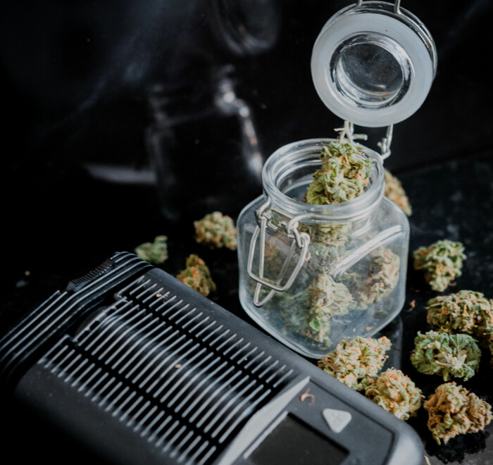 Vaporizer neben einem Glas gefüllt mit Cannabisblüten auf einem schwarzen Untergrund
