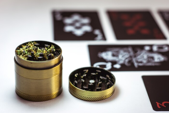 Goldener Grinder welcher mit Cannabis befüllt ist auf einem weißen Tisch mit Karten im Hintergrund