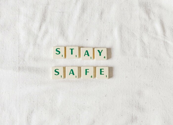 Buchstaben-Plättchen mit grüner Schrift die die Wörter Stay und Safe bilden auf weißem Stoff liegen