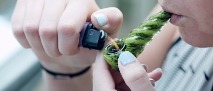 Frau zieht an einer Cannabispfeife die sie mit einem Feuerzeug anzündet