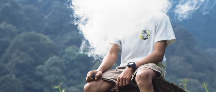 Mann sitzend auf Berg mit Rauchwolke im Gesicht